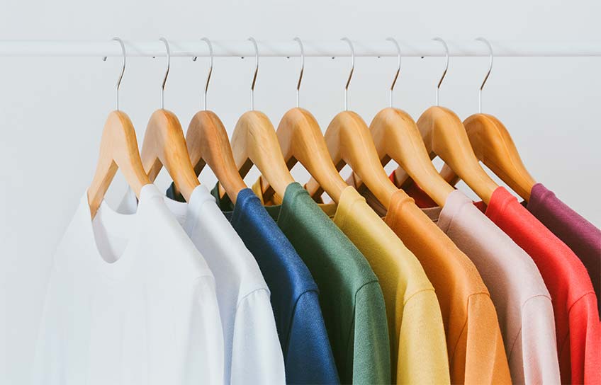 Neun T-Shirt hängen an hölzerne Kleiderbügel exakt nebeneinander und strahlen in den schönsten Farben, nachdem sie in unserer Putzerei fachgerecht gereinigt wurden.